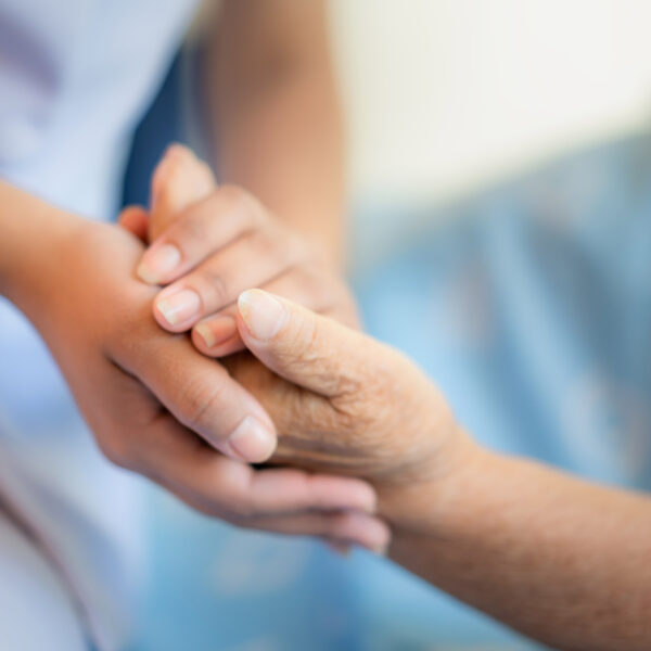 Foto einer Pflegefachkraft, die schützend die Hände einer Patientin hält.